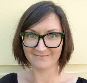 Headshot of a woman with a dark brown bob haircut wearing black framed glasses