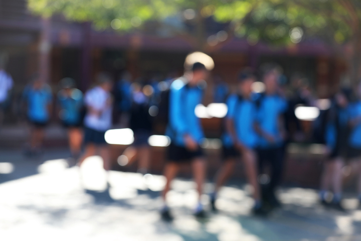 Blurred image of school children walking through a school quadrangle with their backpacks on