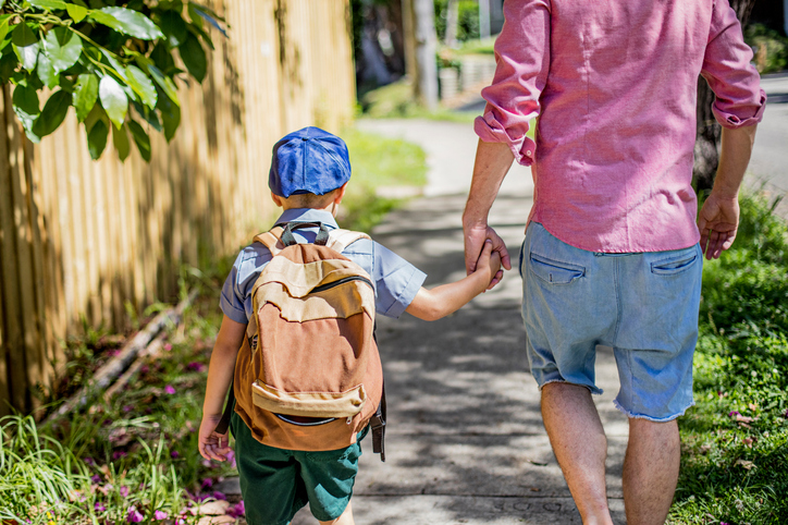 Rear view of a father taking his son to school, they are walking in the street holding hands.