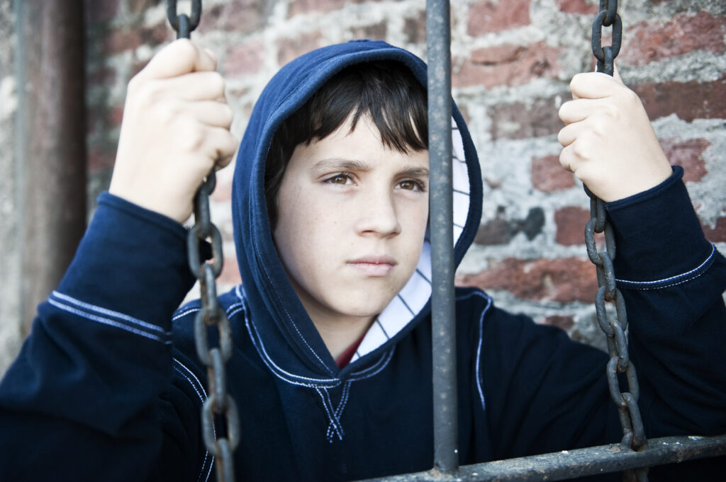 little boy looking through the bars of a juvenile detention centre