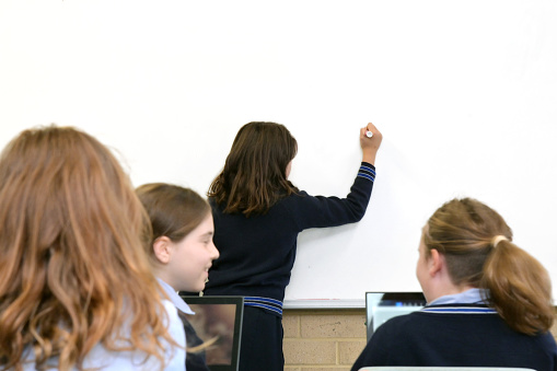 Schoolgirl student writing on a clear whiteboard