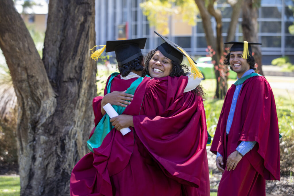 university students hugging while wearing graduation clothing