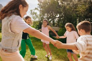 A group of children holding hands and playing together in a sunny park, fostering friendship and outdoor fun.