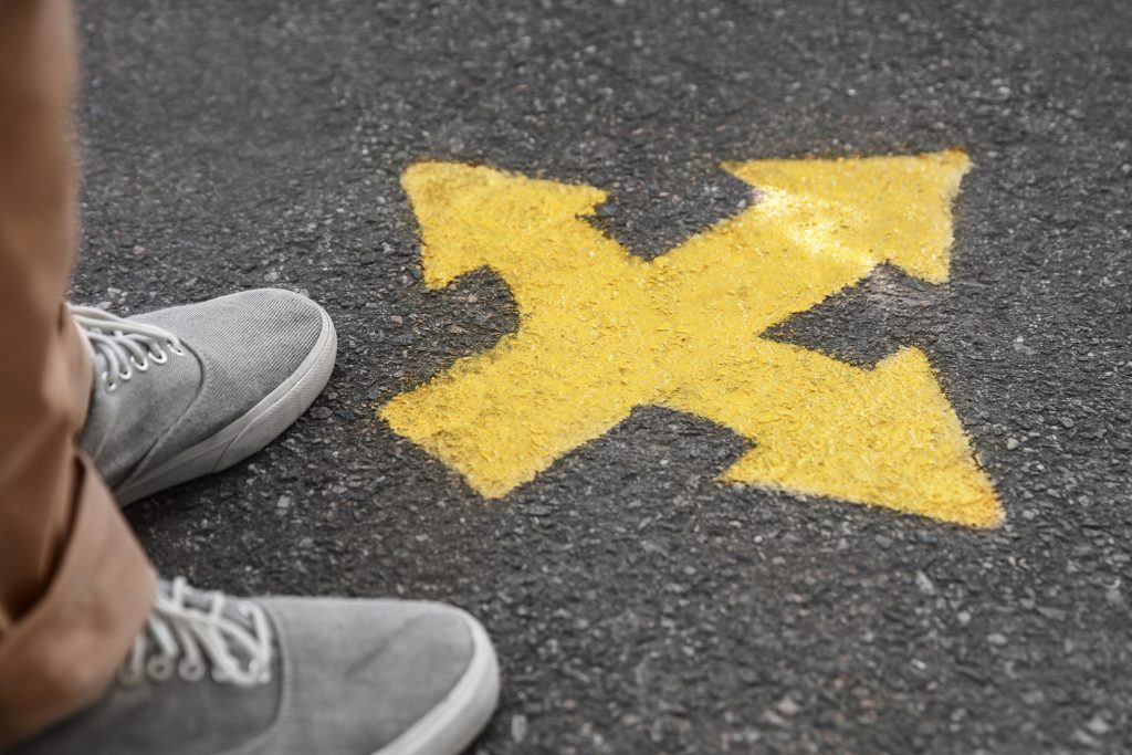 Man standing near arrow with three different direction on asphalt