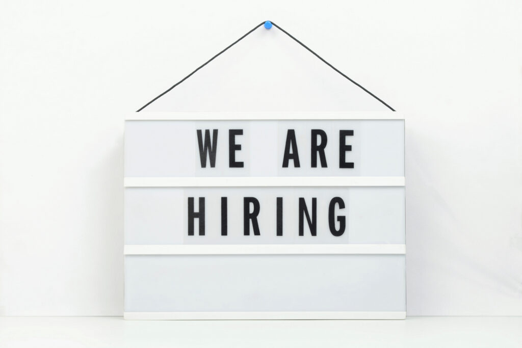 We are hiring sign hanging on a white wall