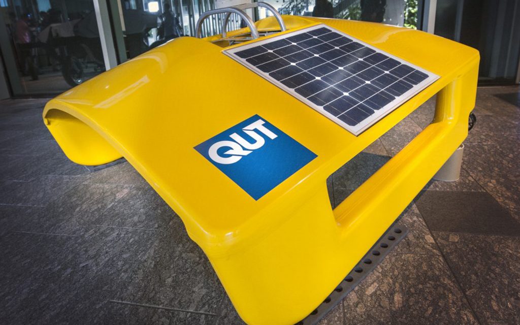 Bright yellow floating robot on display with QUT logo