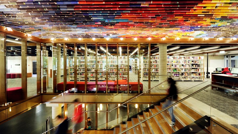 Inside a University Library showing bookshelves and blurred people walking down stairs.