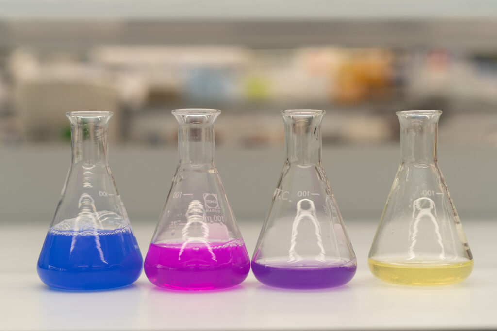 Beakers filled with protein based textile dyes in blue, magenta, purple and yellow