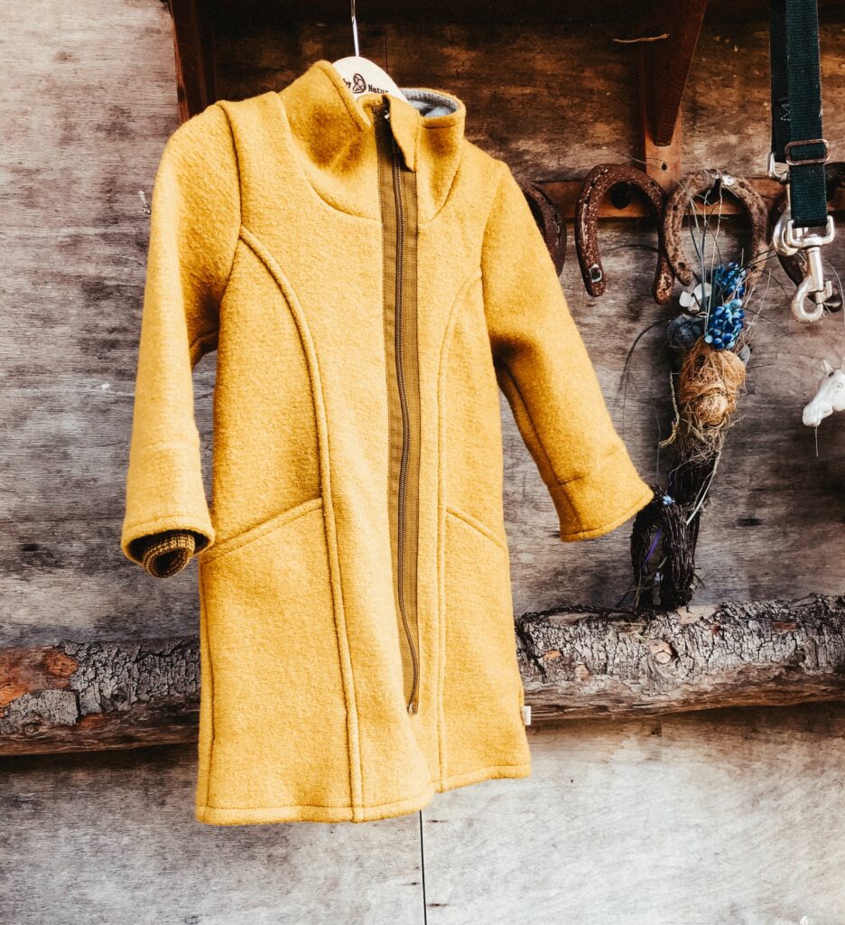 Yellow merino wool coat hangs on a wooden background next to rusted horeshoes